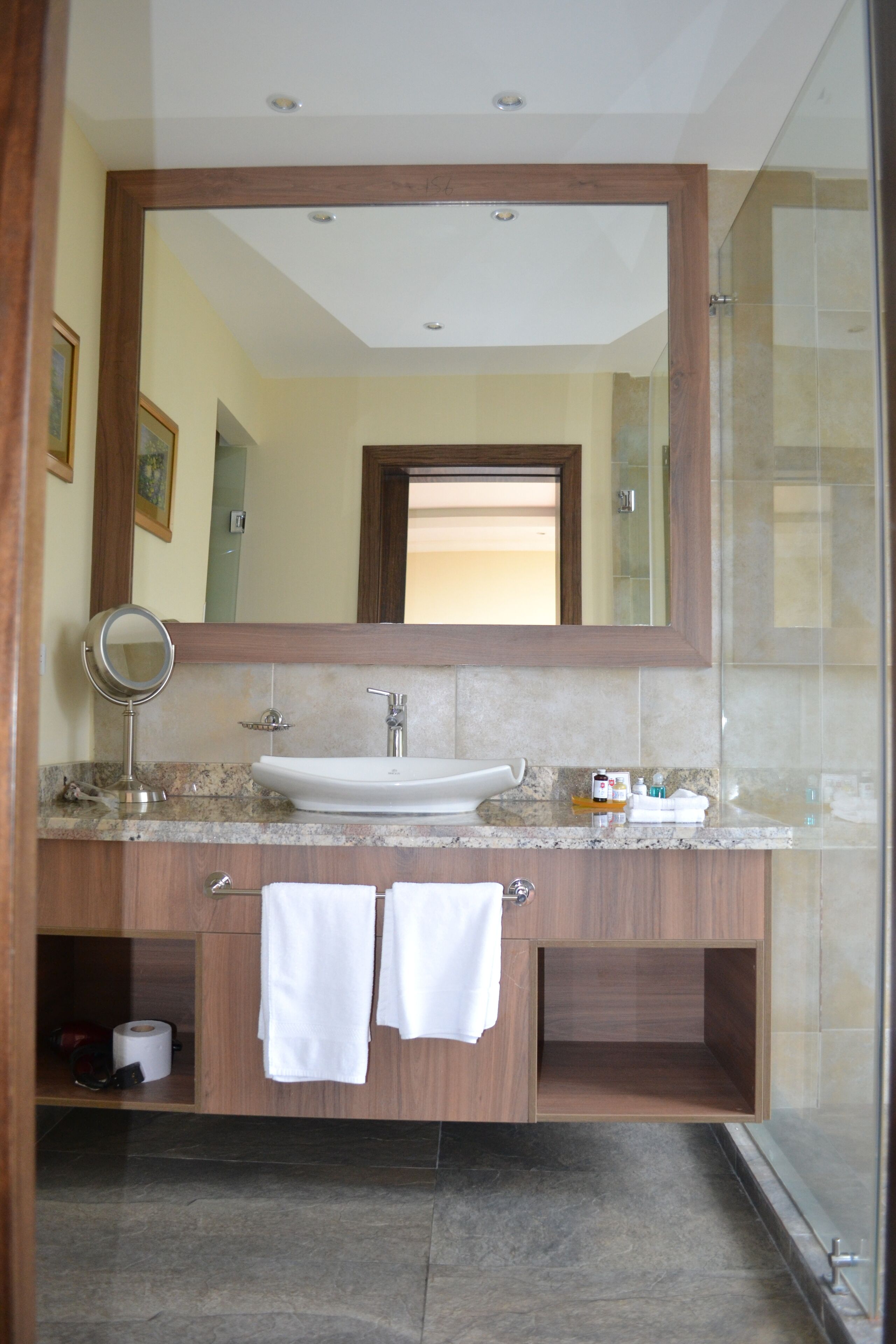 A bathroom with a wooden vanity, a sink, a mirror, and a glass shower enclosure.