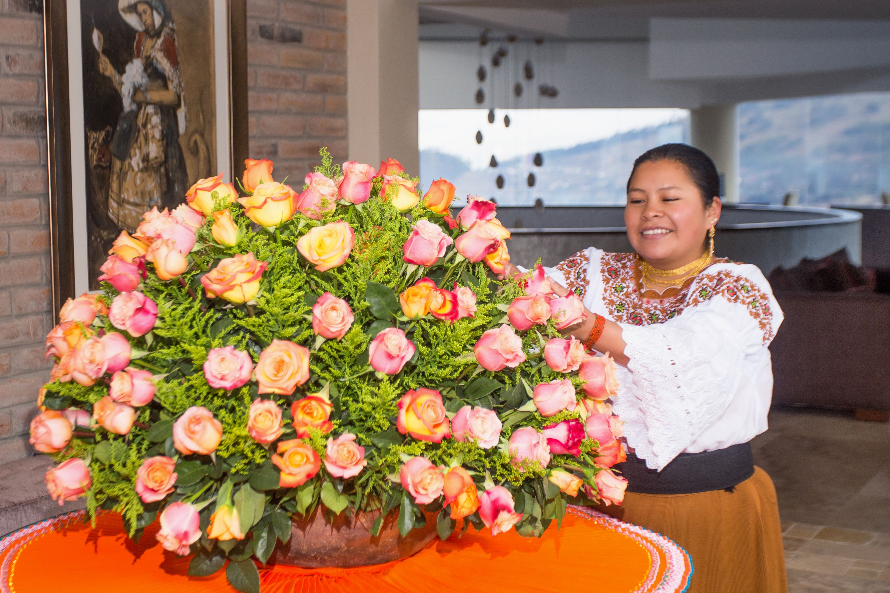 A large floral arrangement in a room with a brick wall and a painting.
