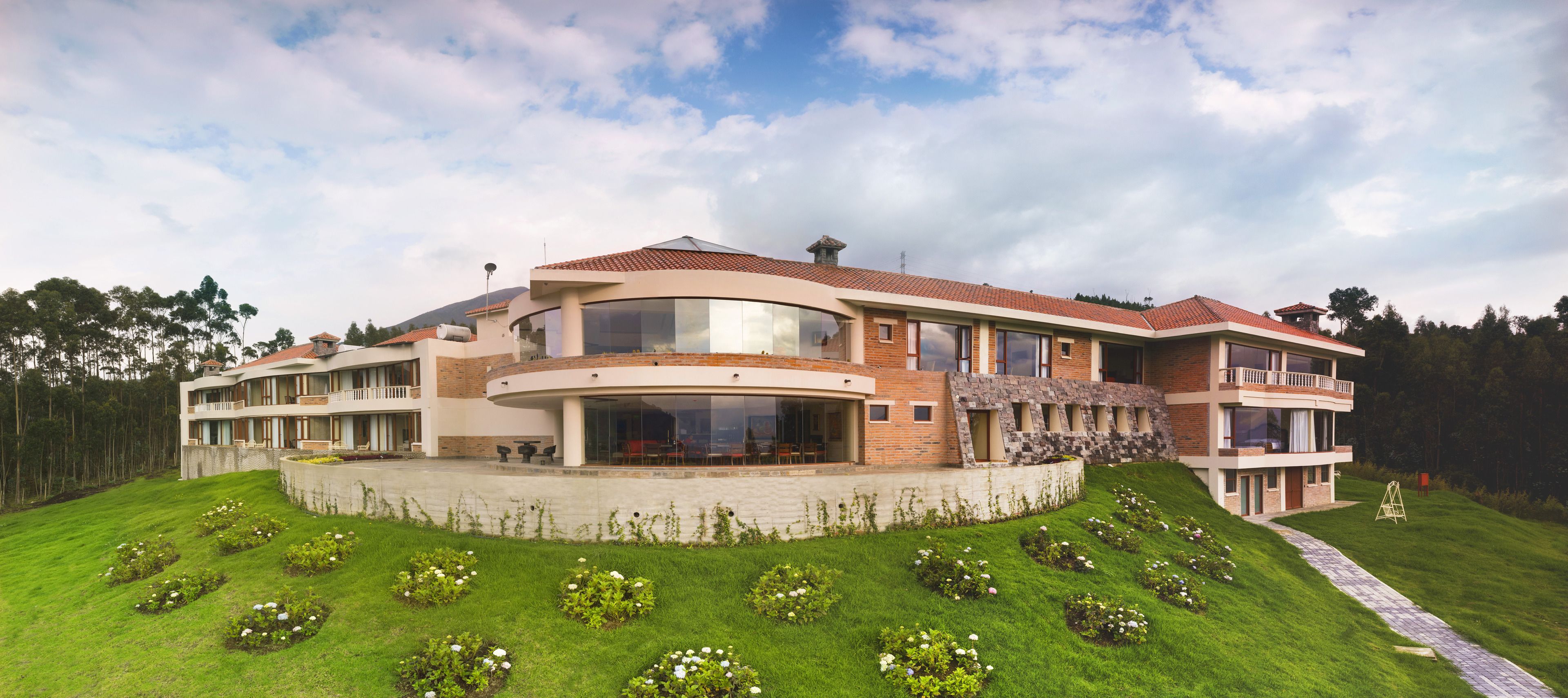 Una casa moderna de varios pisos con techo curvo, ventanas amplias y un césped cuidado con flores.