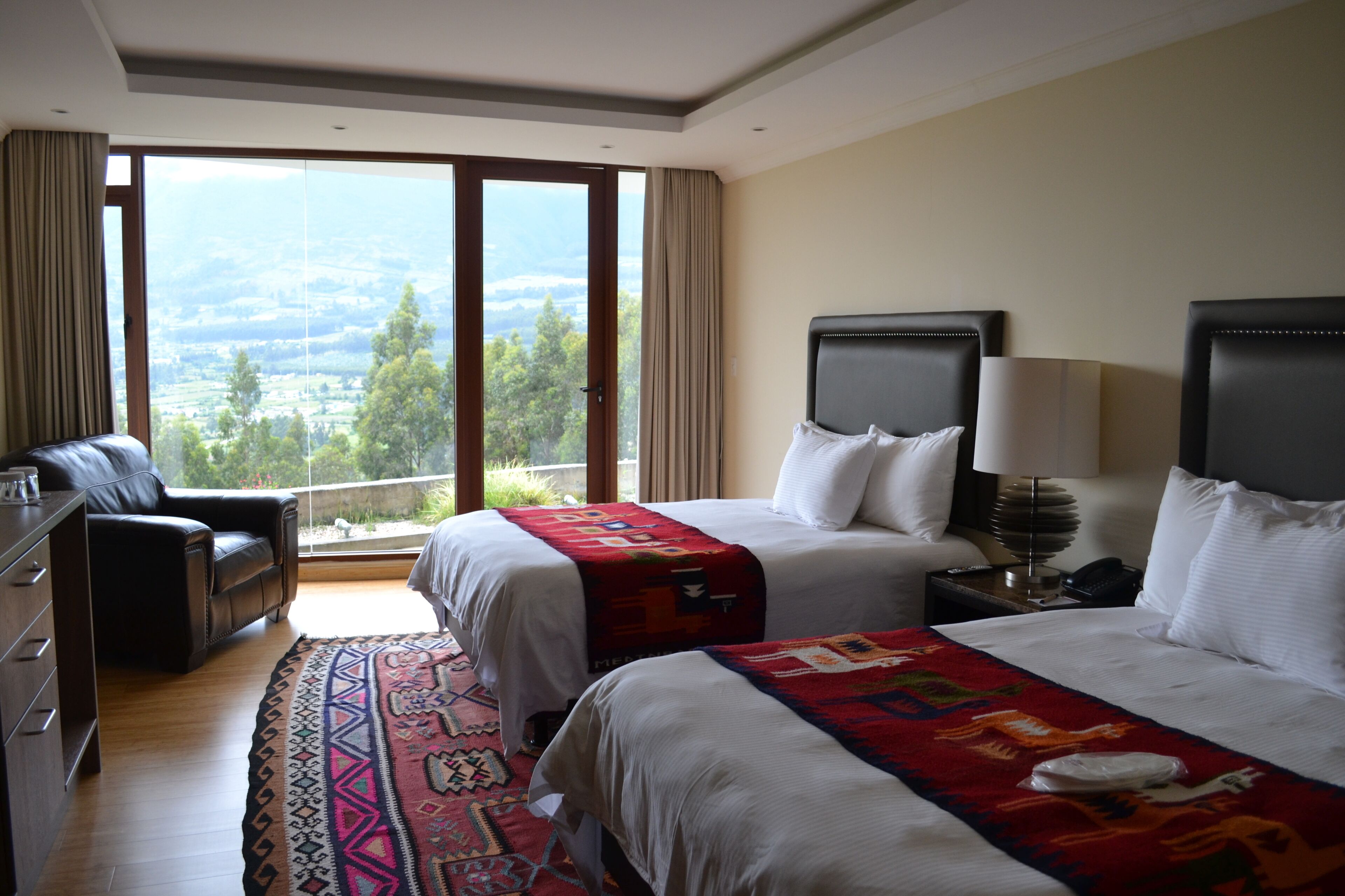 Habitación de hotel con dos camas, un escritorio y vistas al exterior.
