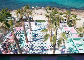 A beachside resort with outdoor seating areas, palm trees, and a view of the ocean.