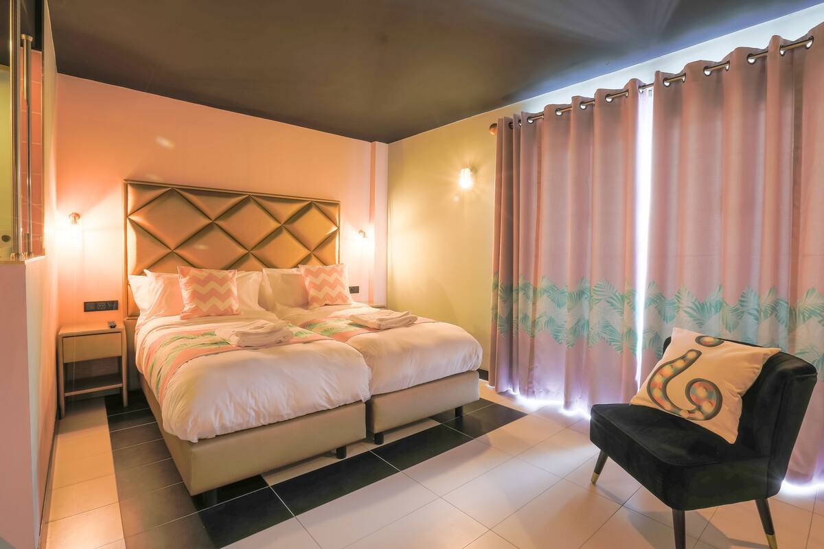 A bedroom with a bed, a chair, a nightstand, and curtains.