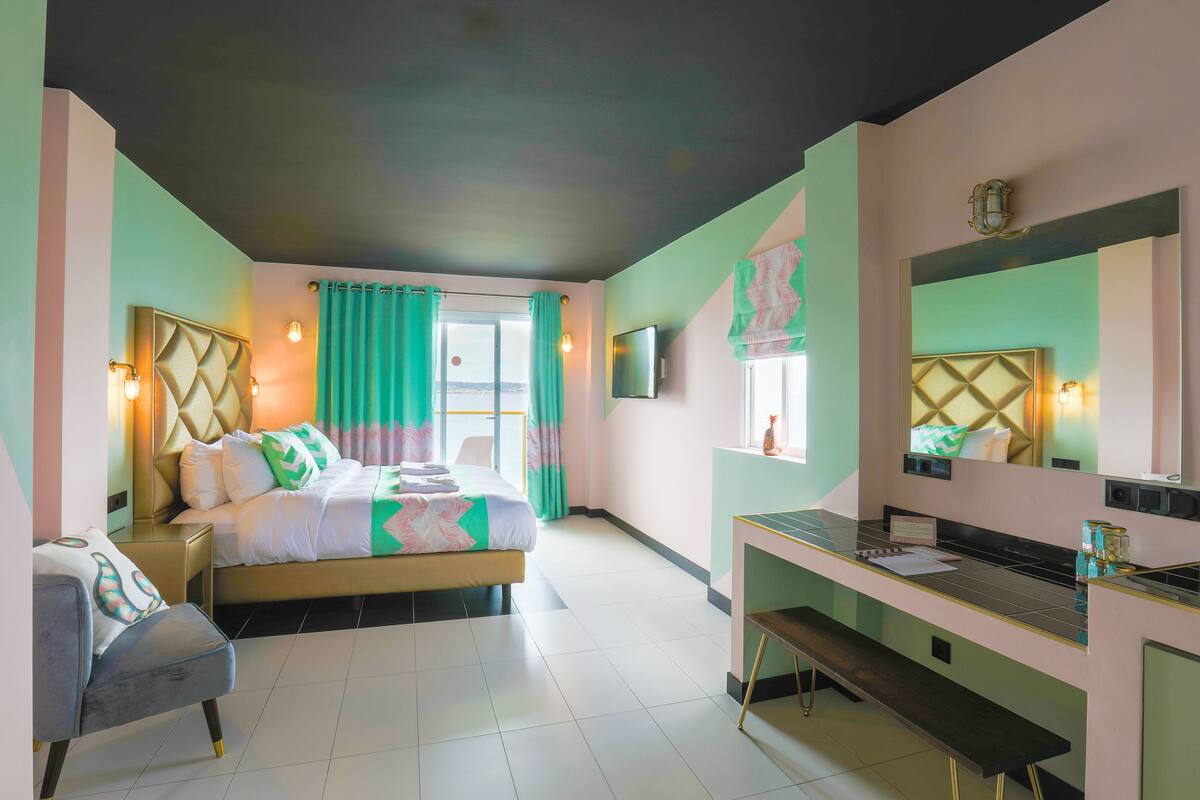 A modern bedroom with a bed, bedside table, bench, and a desk area with a mirror.