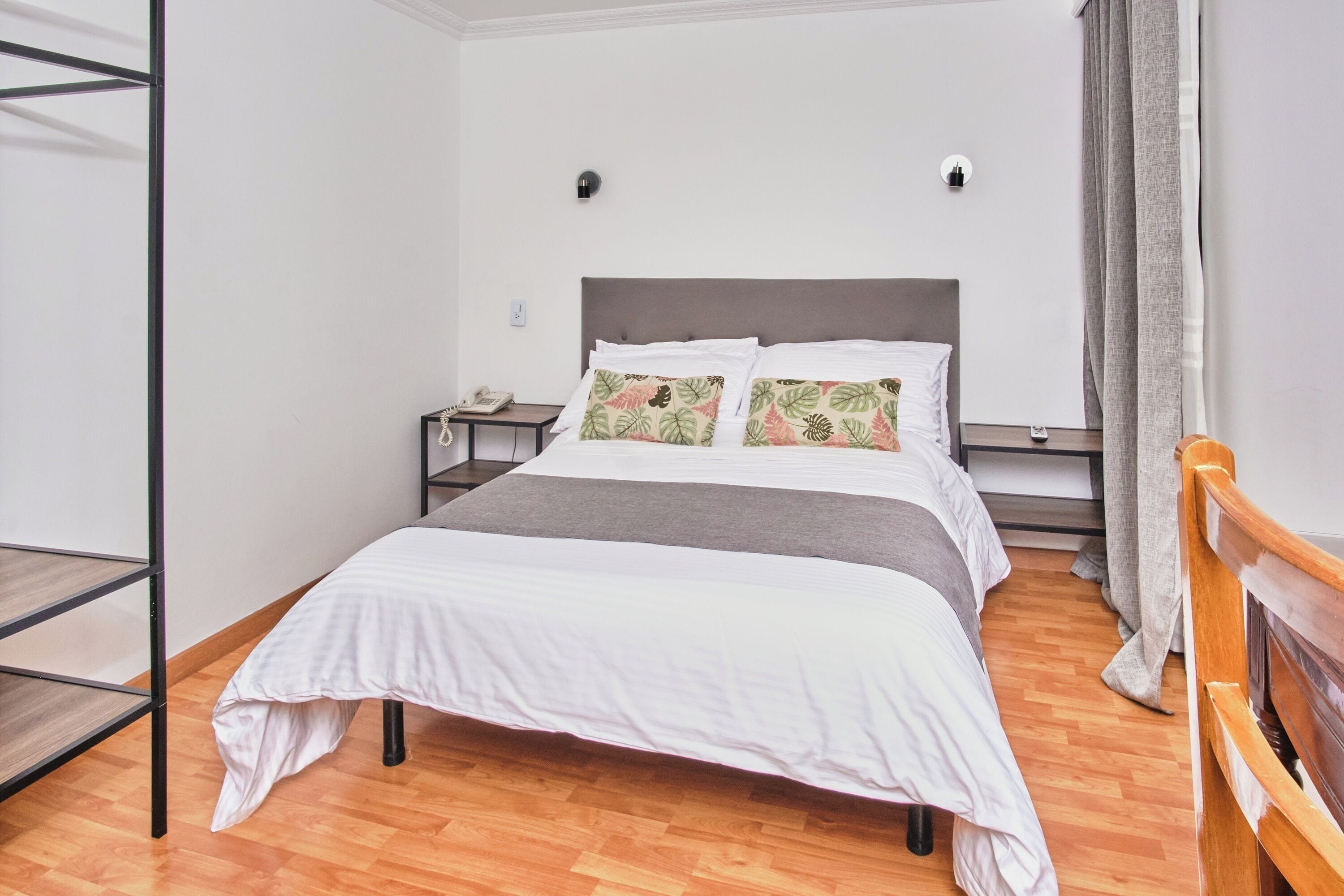 Una camera da letto ordinata con un letto, un comodino, una lampada a parete e un pavimento in legno.