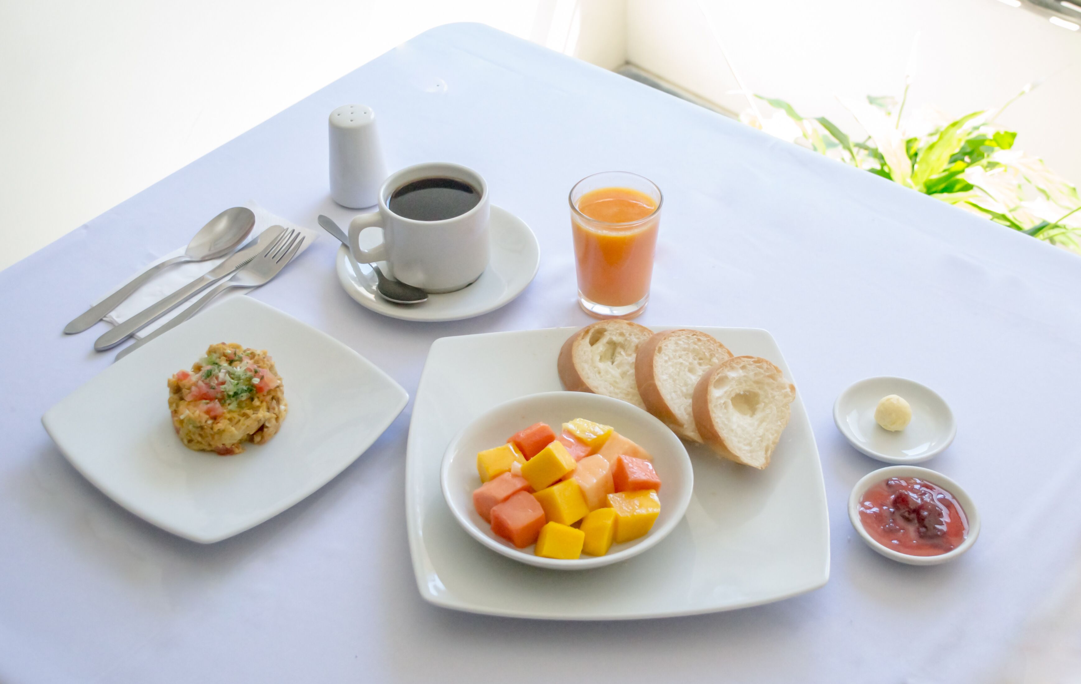 Un desayuno con huevos revueltos, tostadas, fruta, una taza de café y un vaso de jugo de naranja.