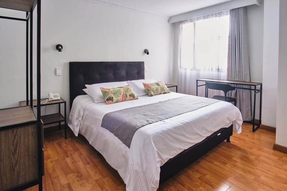 A modern bedroom with a large bed, a desk, and a window with curtains.