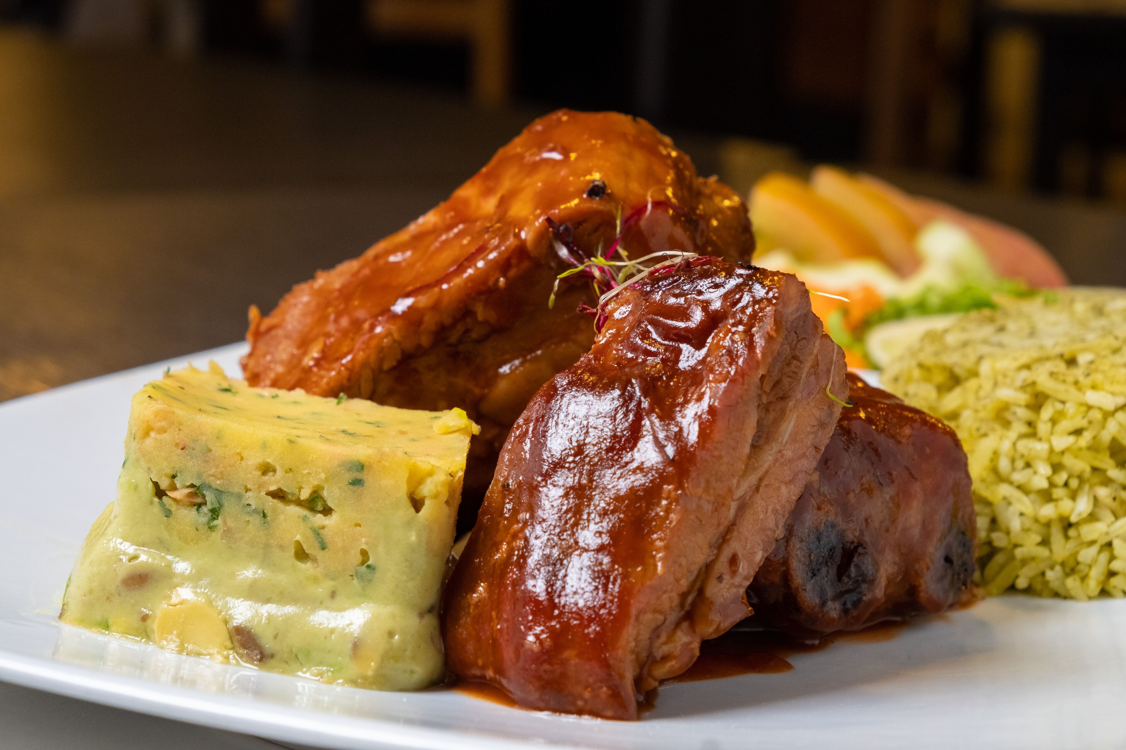 A plate with a glazed meat, a slice of quiche, and a side of rice.