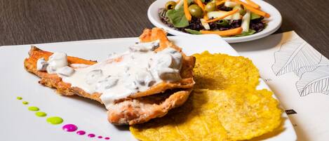 Een bord met eten, getopt met witte saus, een gele chips en een salade met groenten en olijven.