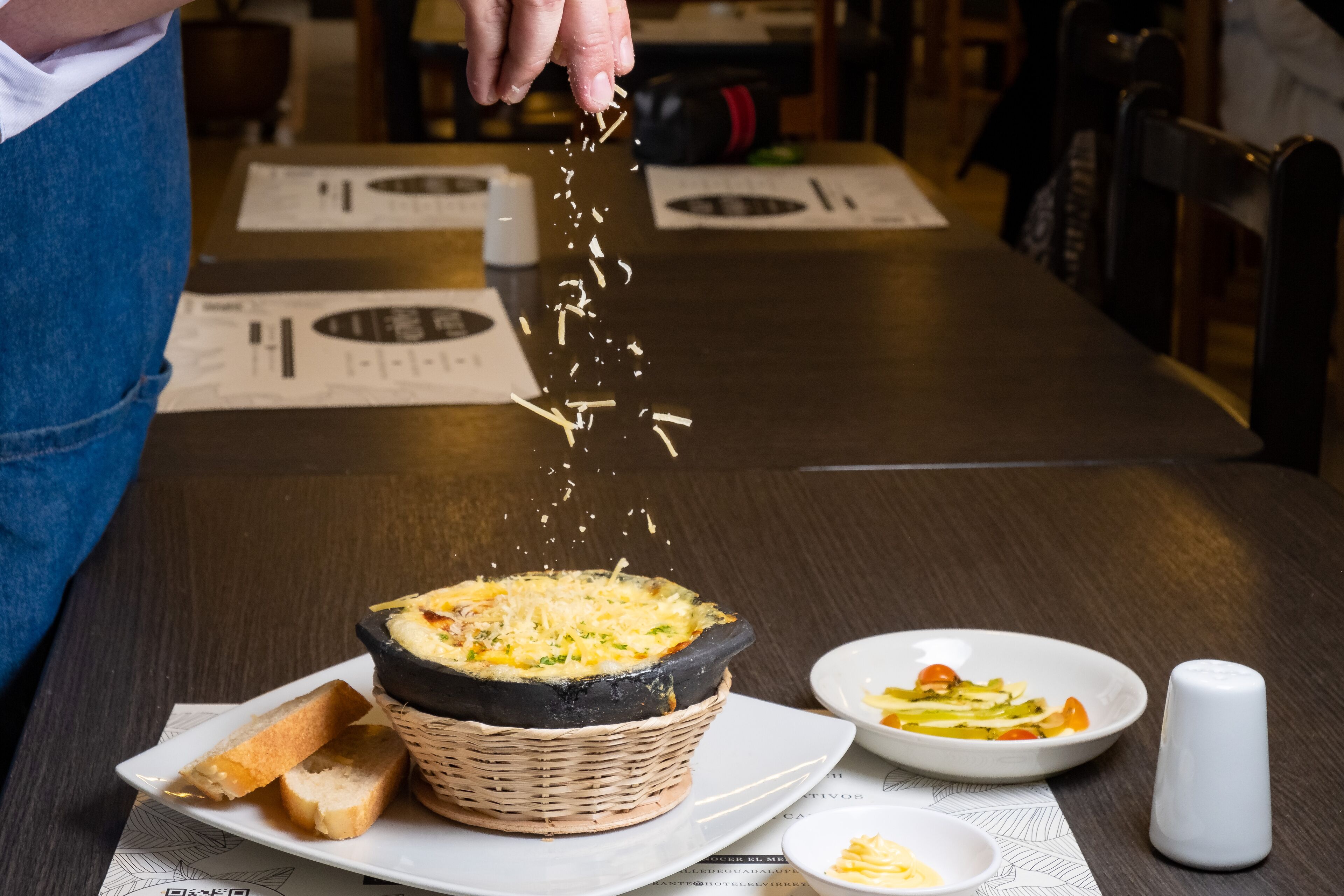 Una persona esparciendo queso sobre un plato en un restaurante.
