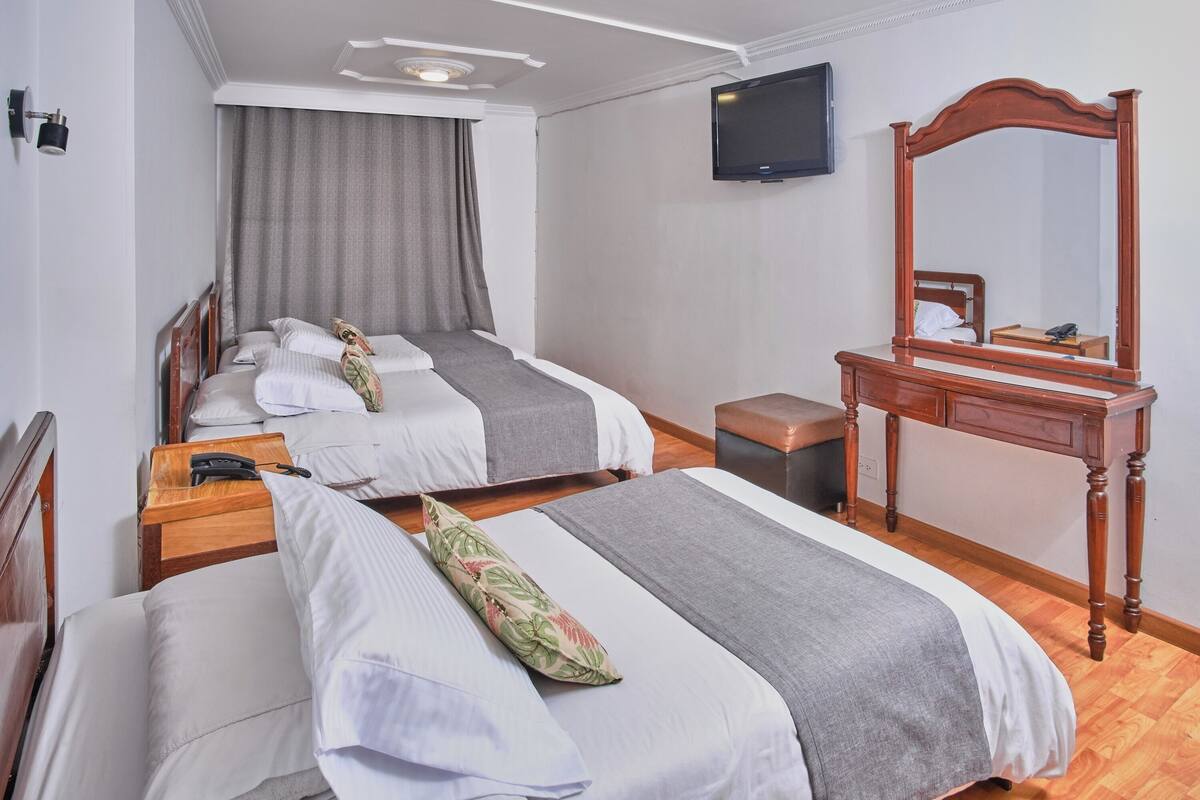 A hotel room with two beds, a wooden dresser, a television, and a mirror.