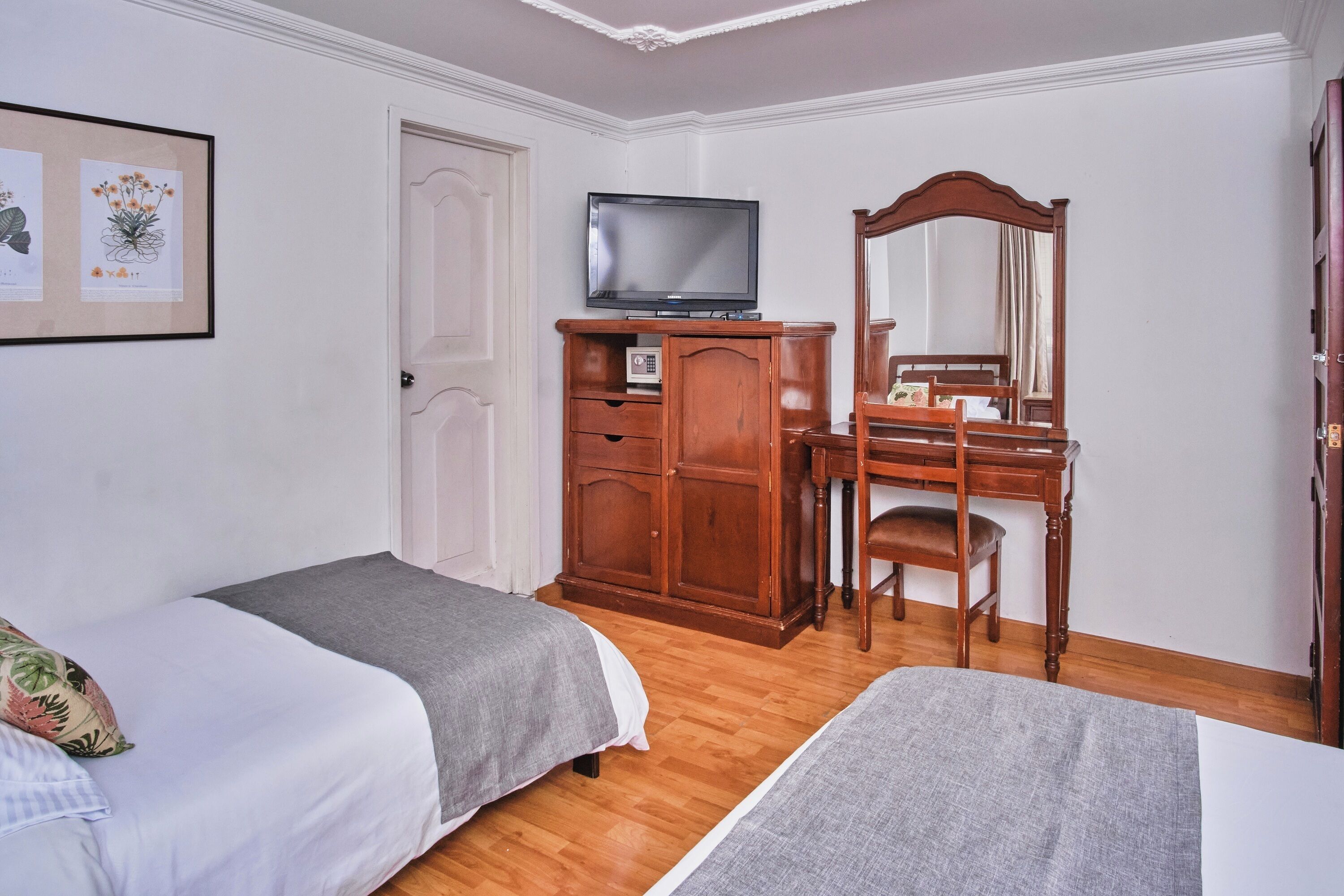 Quarto com duas camas, um guarda-roupa de madeira, uma televisão e um espelho.