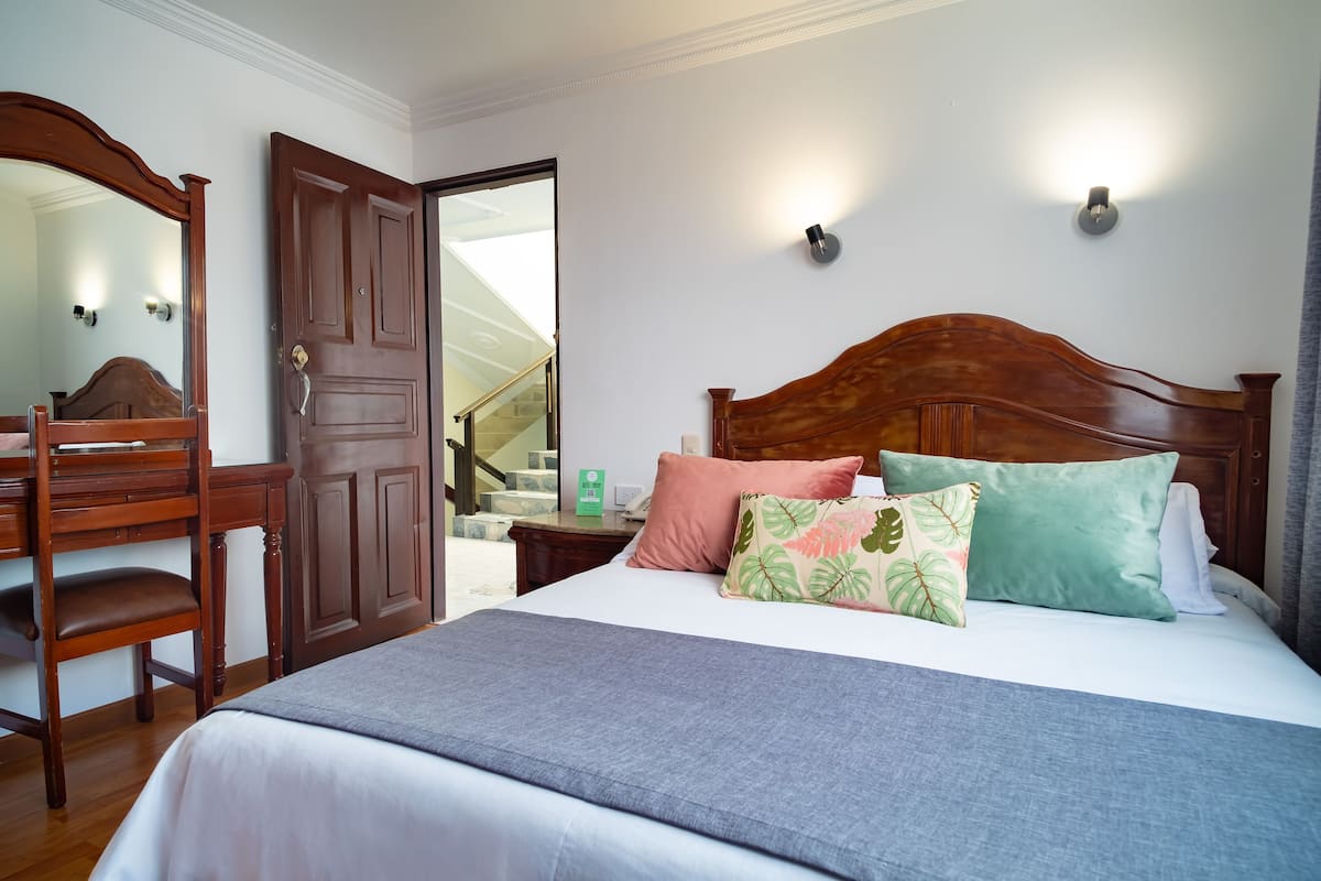 A bedroom with a wooden bed, a nightstand, a dresser, and a mirror.