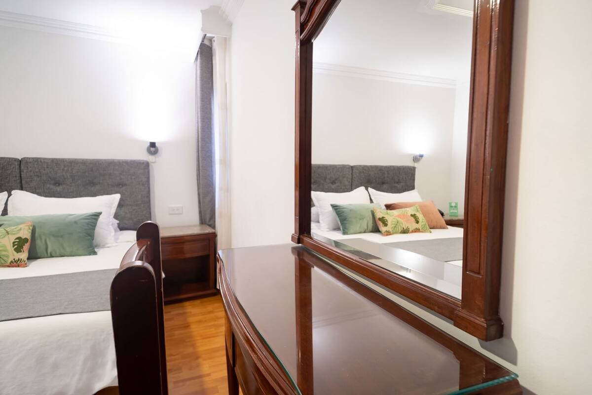A hotel room with two beds, a wooden desk, and a large mirror.