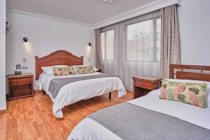 Une chambre d’hôtel avec un lit double, une table de chevet, une commode et une grande fenêtre avec des rideaux.