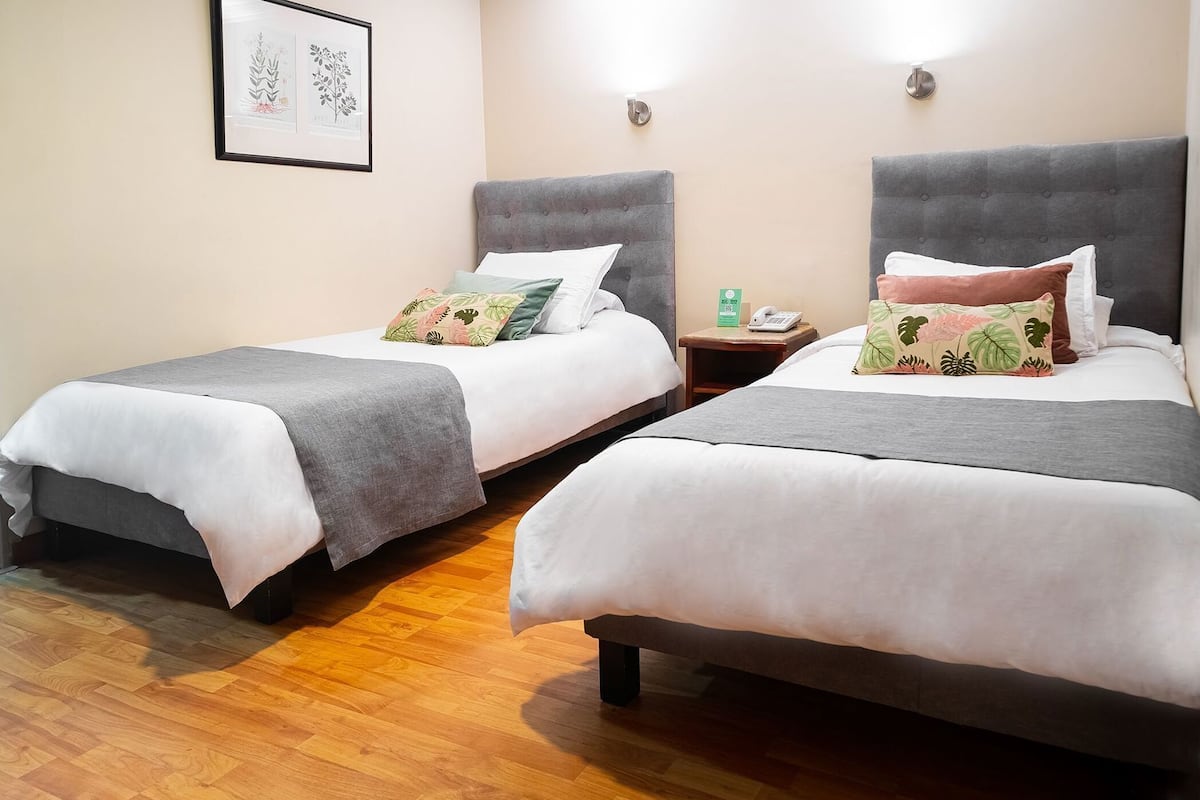 Two twin beds with grey headboards, white bedding, and a wooden floor.