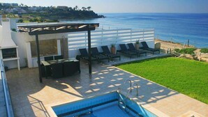 A pool area with a view of the ocean, outdoor seating, and a pergola. - Blue Coral Beach Villas (Paphos)