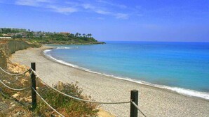 A coastal beach with a clear view of the ocean and a distant shoreline with buildings. - Blue Coral Beach Villas (Paphos)