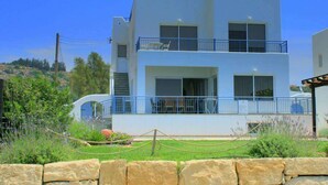 A modern two-story building with a balcony, large windows, and a stone wall in the foreground. - Blue Coral Beach Villas (Paphos)