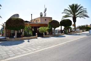 A building with a satellite dish, palm trees, and a sign indicating a business. - Dimma Seaside Houses (Chlorakas)