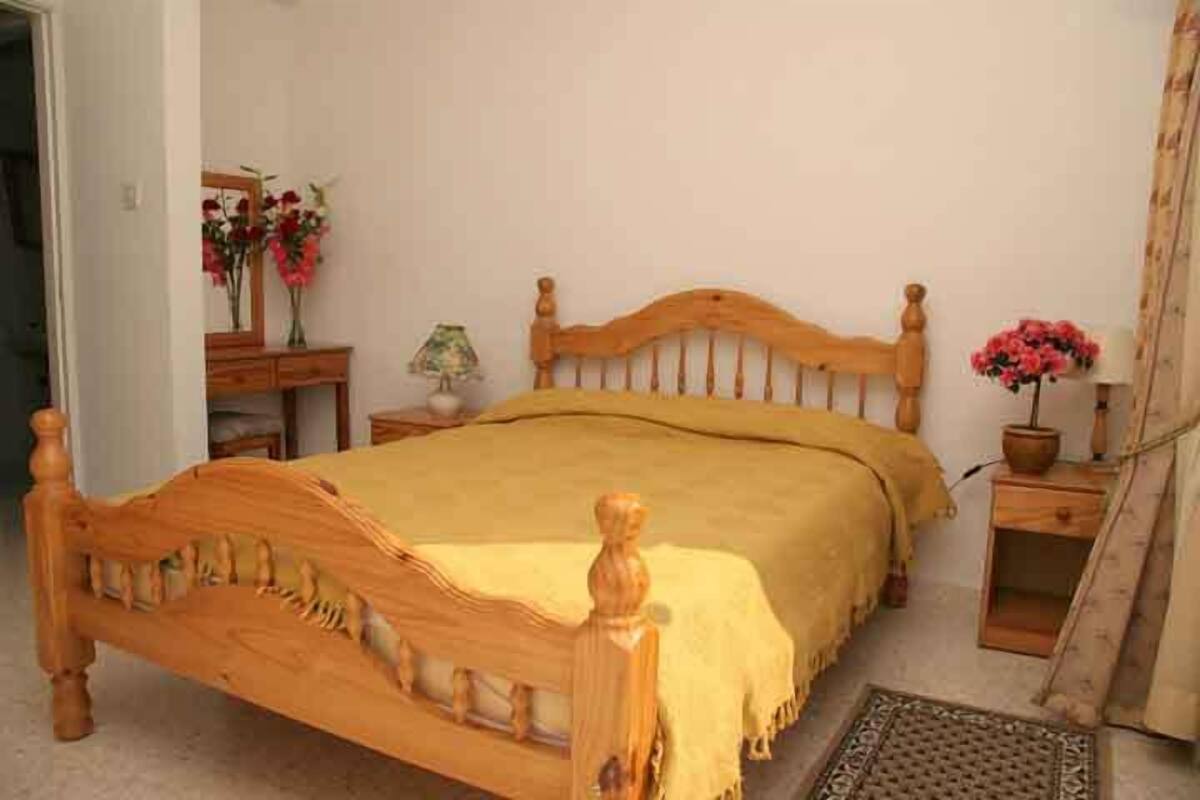 Un lit en bois avec une couvre-lit jaune, une table de chevet avec une lampe et un miroir accroché au mur.