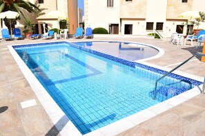 Una piscina al aire libre, sombrillas, sillones reclinables de piscina