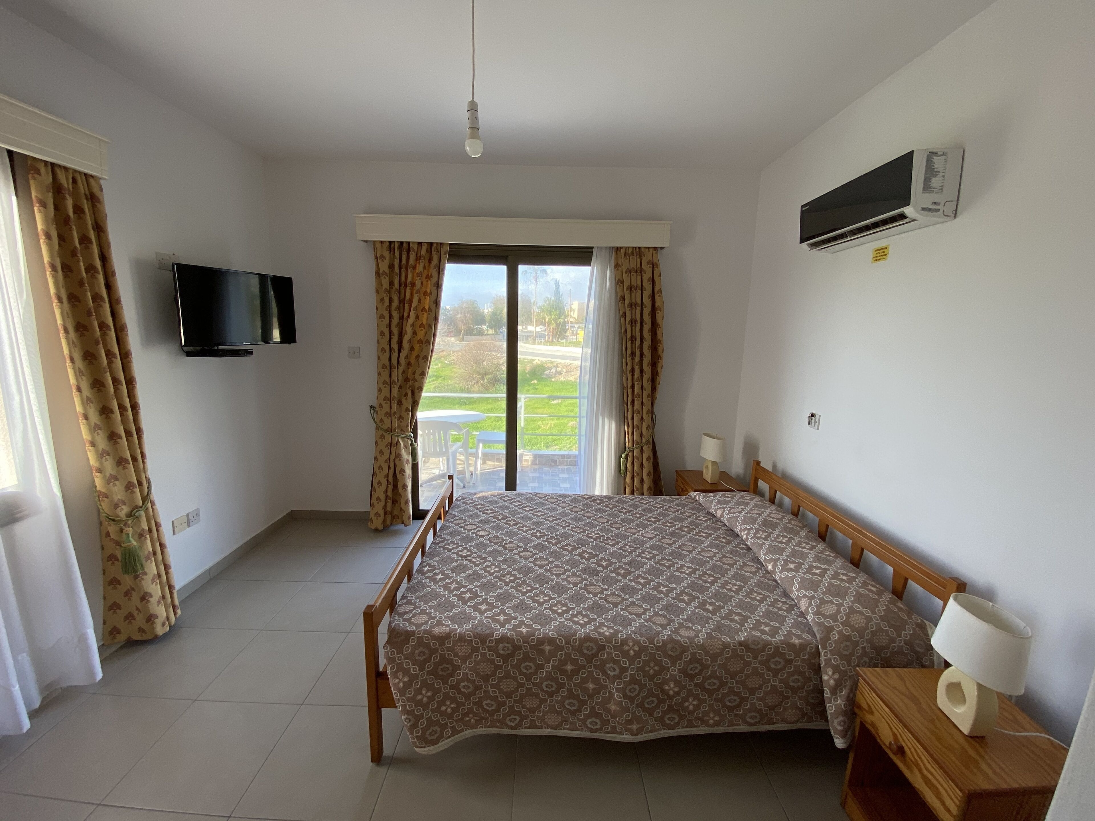 A bedroom with a bed, a TV, an air conditioner, and a view of the outdoors.