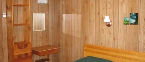 A wooden-paneled room with a bed, a desk, and a chair.