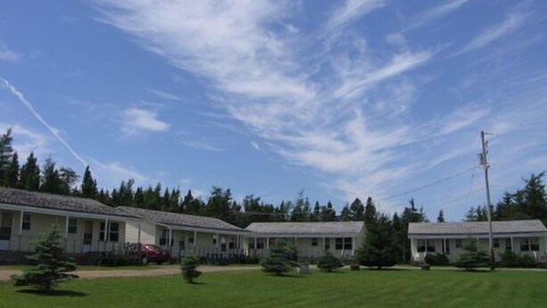 A row of single-story buildings with a flat roof, surrounded by a grassy area and trees. - Joyce's Motel & Cottages (St. Peters)