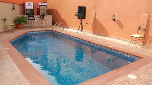Ein Schwimmbecken mit Fliesenrand, ein Barbereich mit Hockern und ein Kübelpflanze.