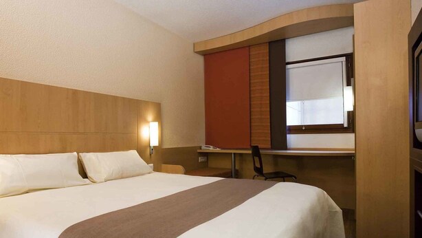 Ein Hotelzimmer mit einem großen Bett, einem Schreibtisch, einem Stuhl und einem Fernseher.