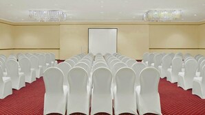 Ein Konferenzraum mit Reihen weißer Stühle, einem roten Teppich und einer Tafel an der Wand.
