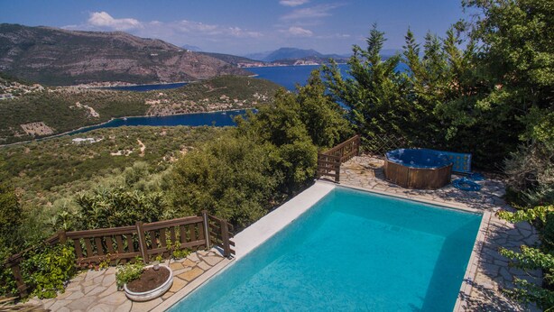 A swimming pool with a wooden deck, surrounded by lush greenery and a scenic view of a lake and mountains. - Arethousa Villas (Lefkada)