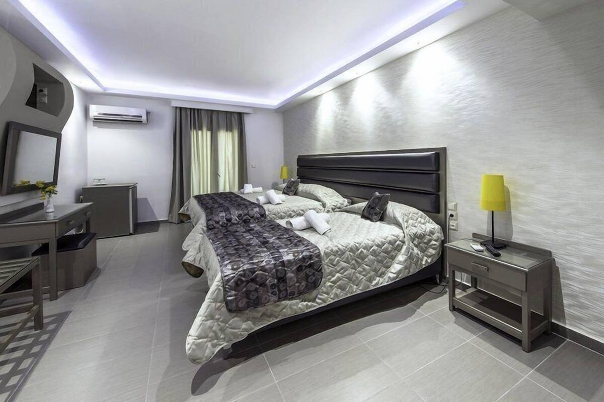 A modern hotel room with a large bed, a desk, a chair, and a bedside table with a lamp.