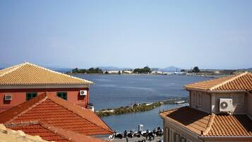 A coastal town with buildings featuring red-tiled roofs, a body of water, and a distant mountain range.