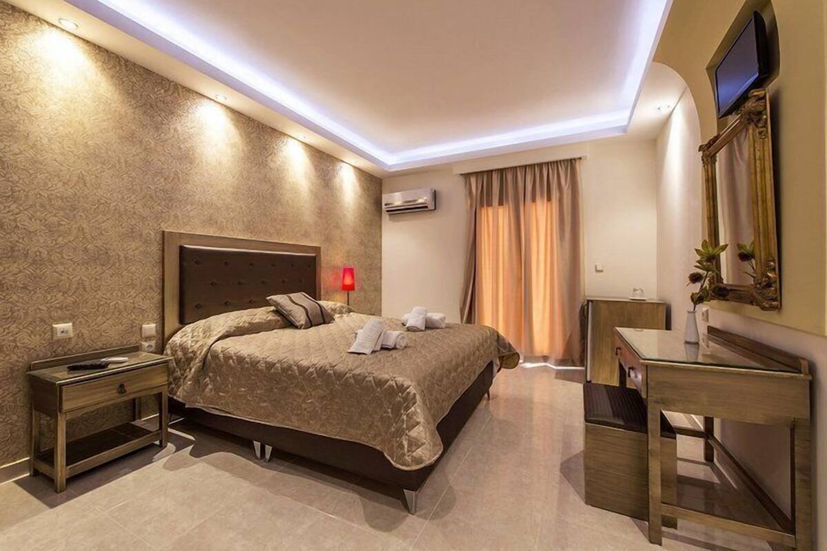 A modern hotel room with a large bed, bedside tables, a desk, and a flat-screen TV mounted on the wall.