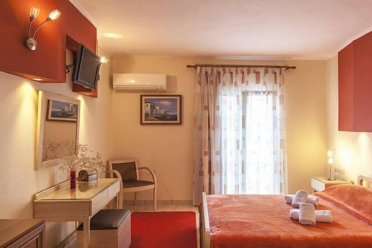 A hotel room with a bed, a desk, a chair, a TV, and a window with curtains.
