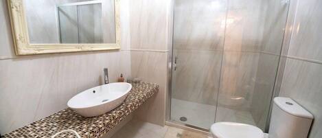 Un baño con lavamanos blanco, un espejo grande, cabina de ducha de vidrio y un inodoro.