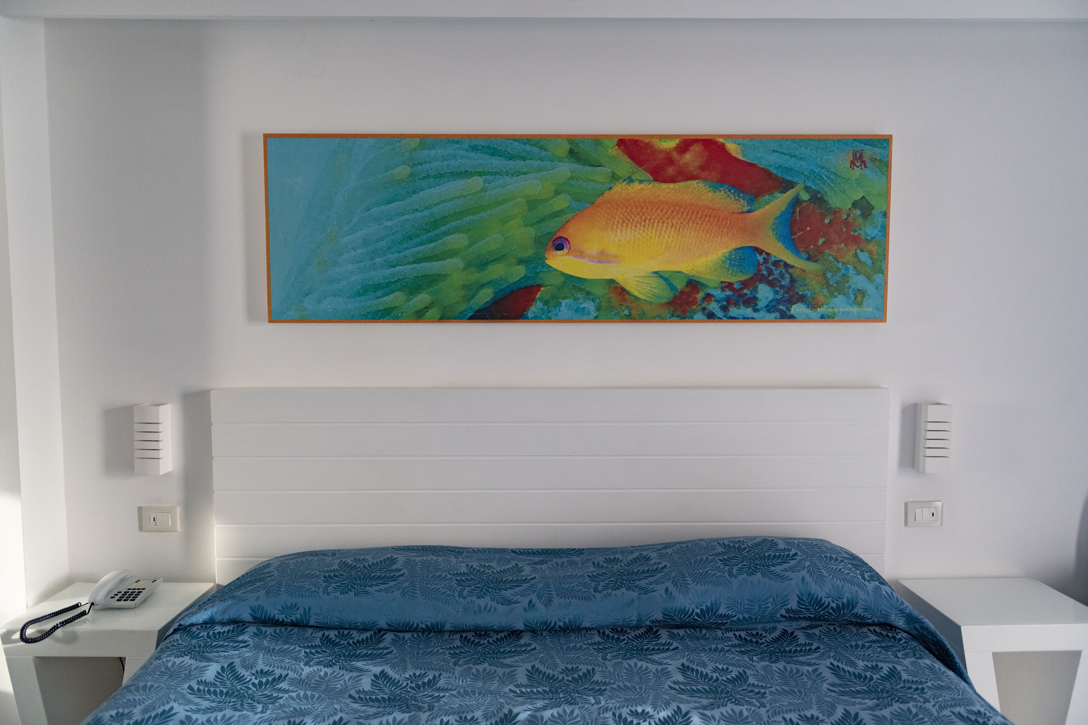 Ein Schlafzimmer mit einem Bett, einem Bild von einem Fisch und einem weißen Nachttisch mit einem Telefon.