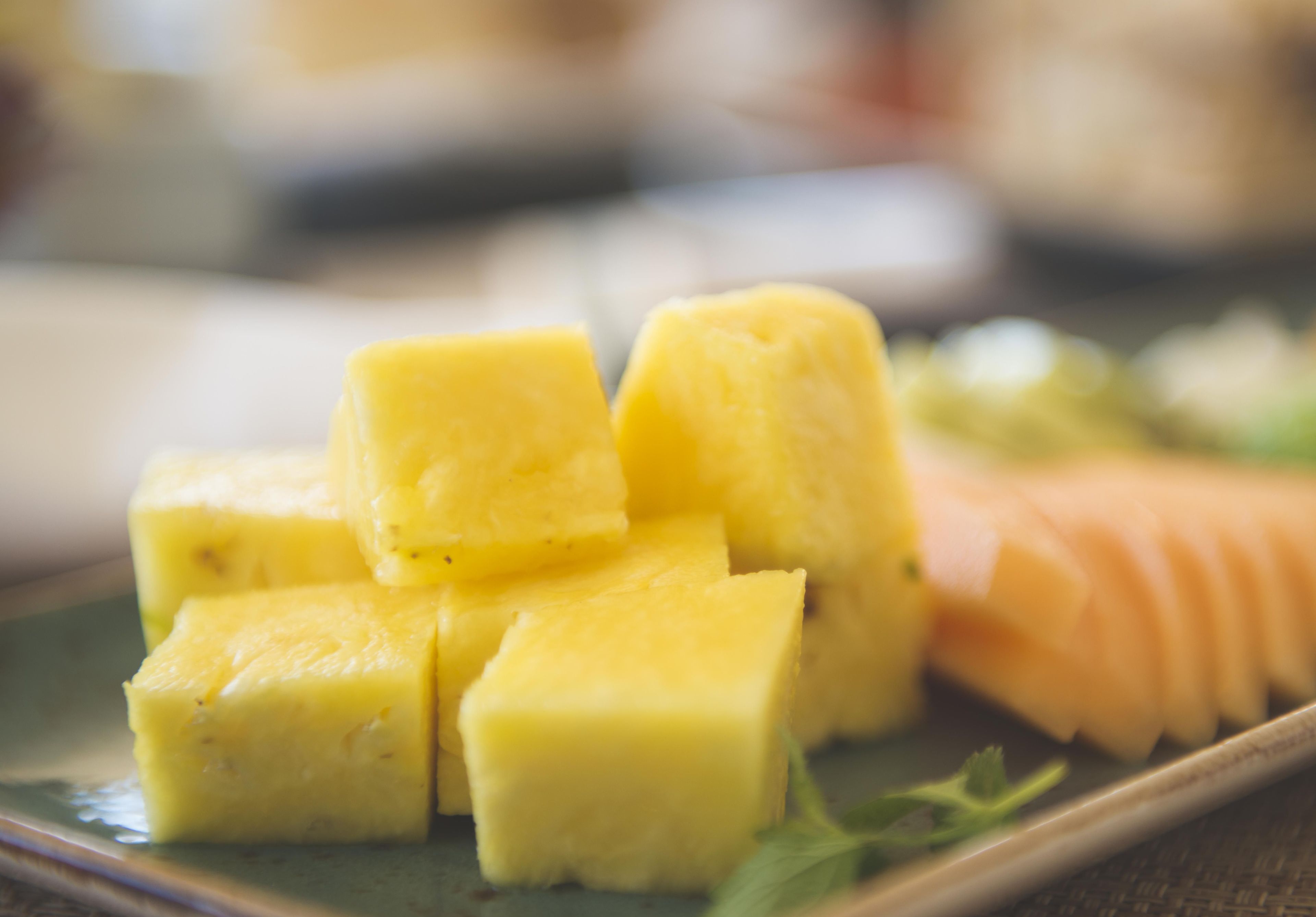 A plate with pineapple chunks and a carved piece of fruit, possibly melon, on a ceramic plate with a green rim.