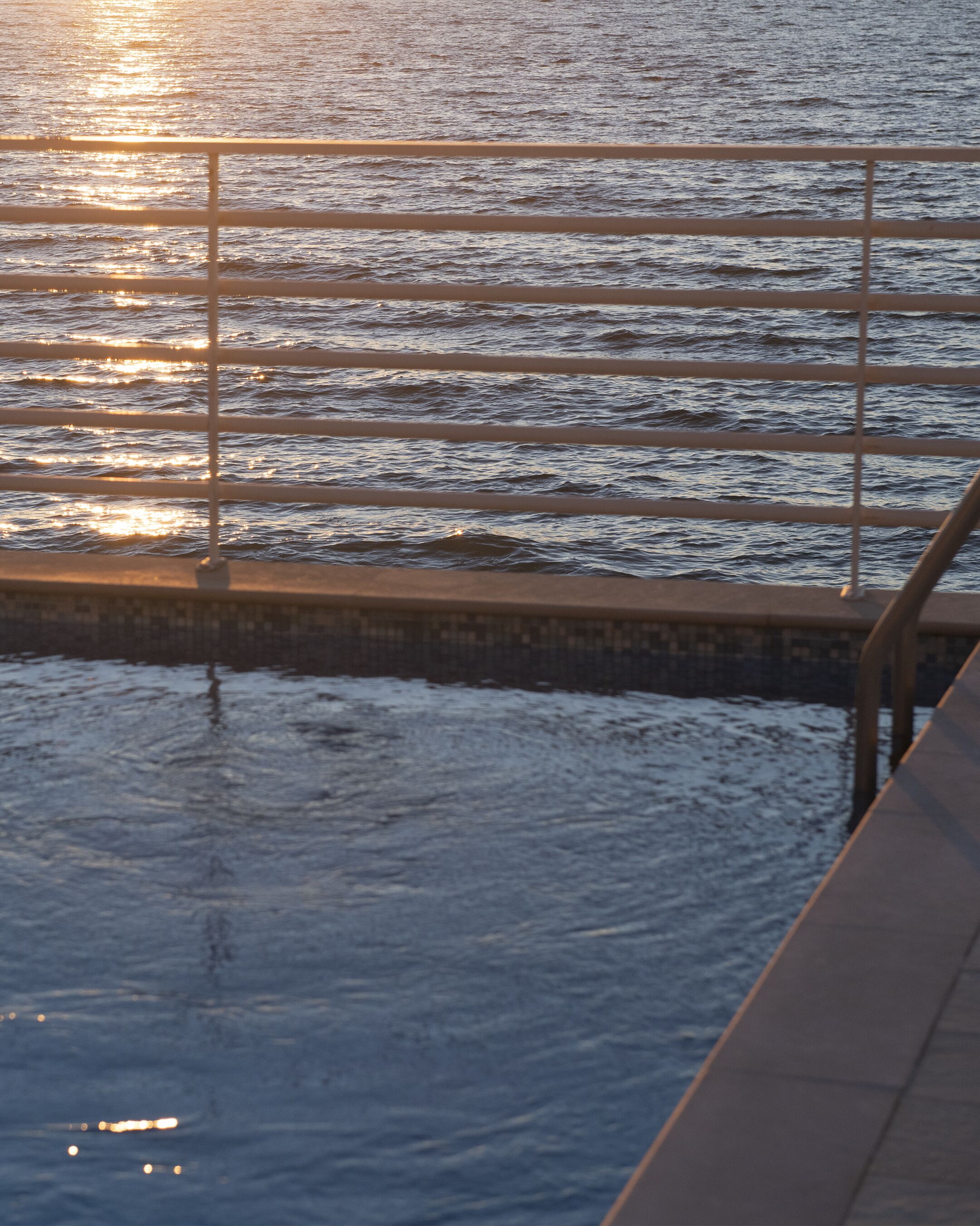 A waterfront view with a metal railing and a tiled walkway.