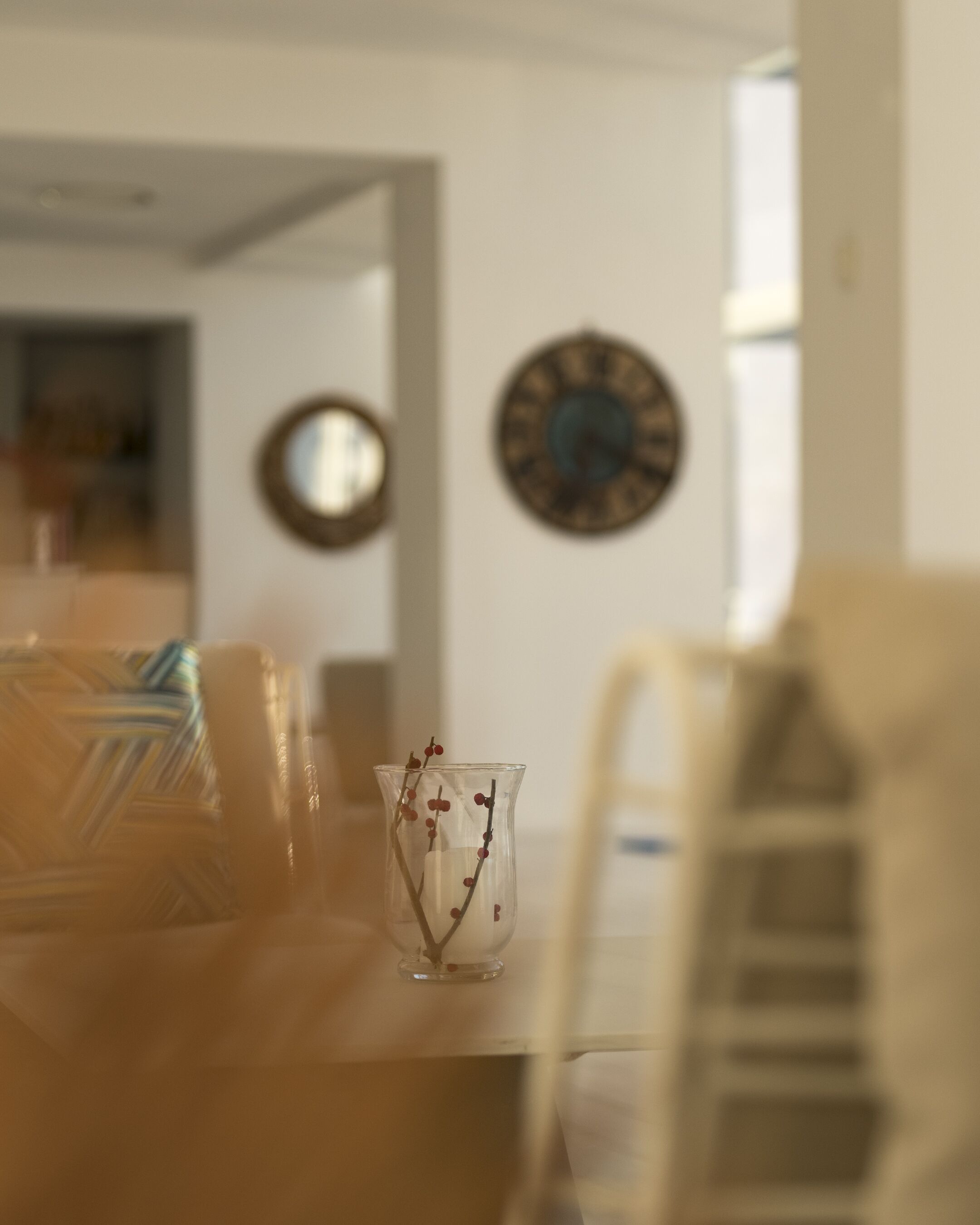 Ein Essbereich mit Tisch, Stühlen und einer Vase mit Zweigen. An der Wand hängen Uhren.