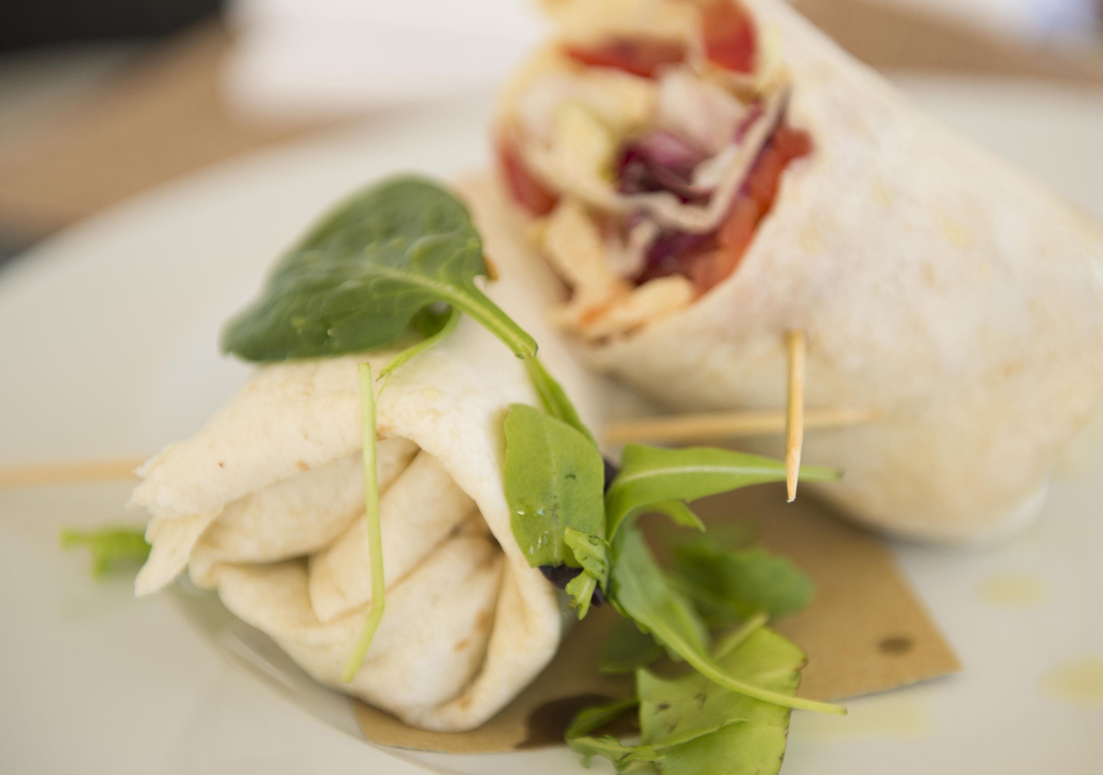 A burrito with a toothpick, wrapped in a tortilla, and garnished with greens.