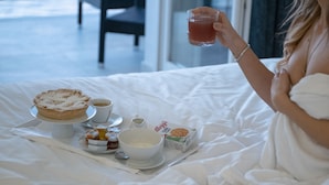 Una cama con un carrito de desayuno que contiene una tarta, café, un tazón de cereal y salsas.