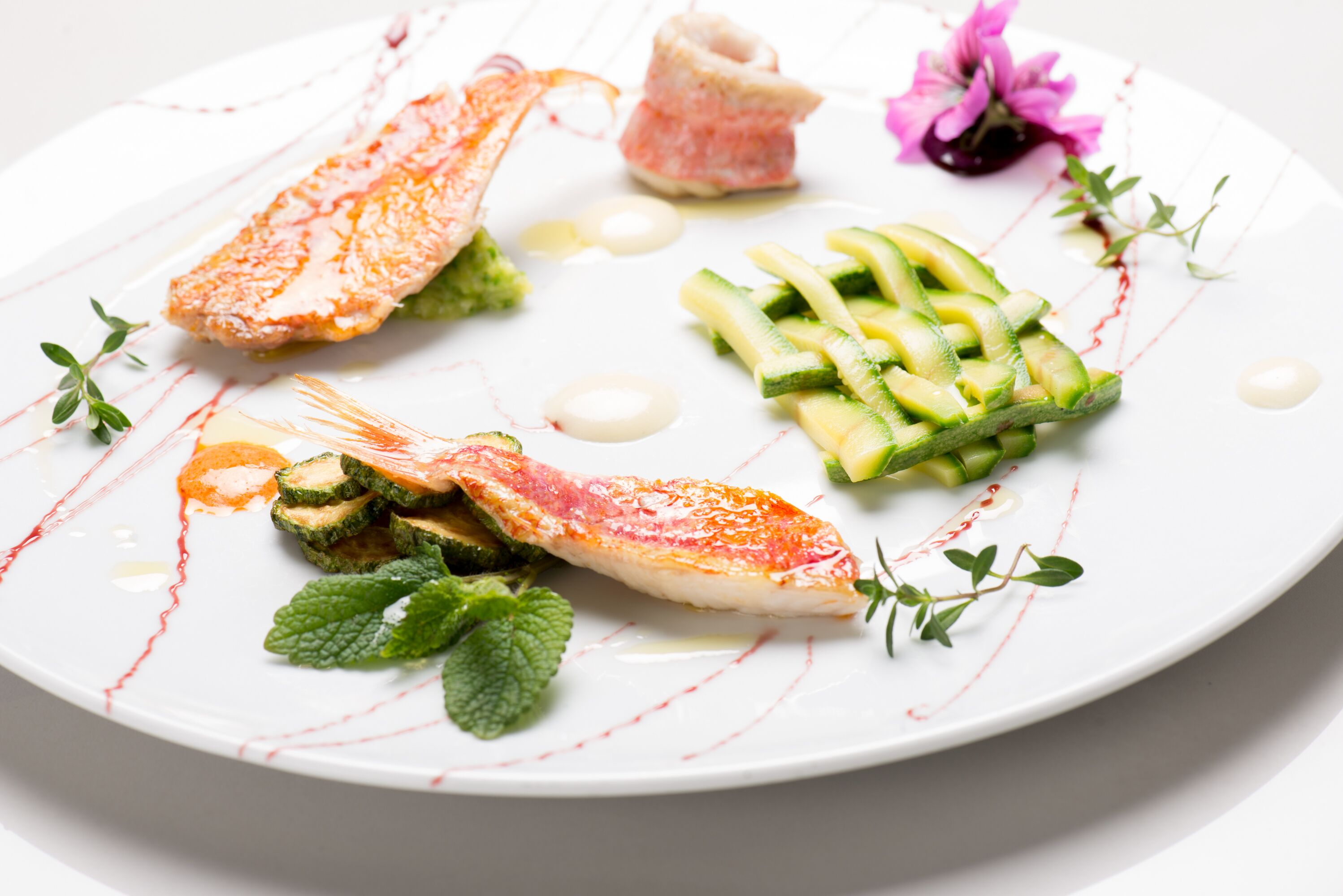 A white plate with a fish fillet, cucumber slices, and a small flower.