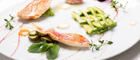 Un plato blanco con un filete de pescado, rodajas de pepino y una pequeña flor.