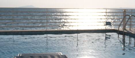 A sunlit pool area with a lounge chair and a metal railing.