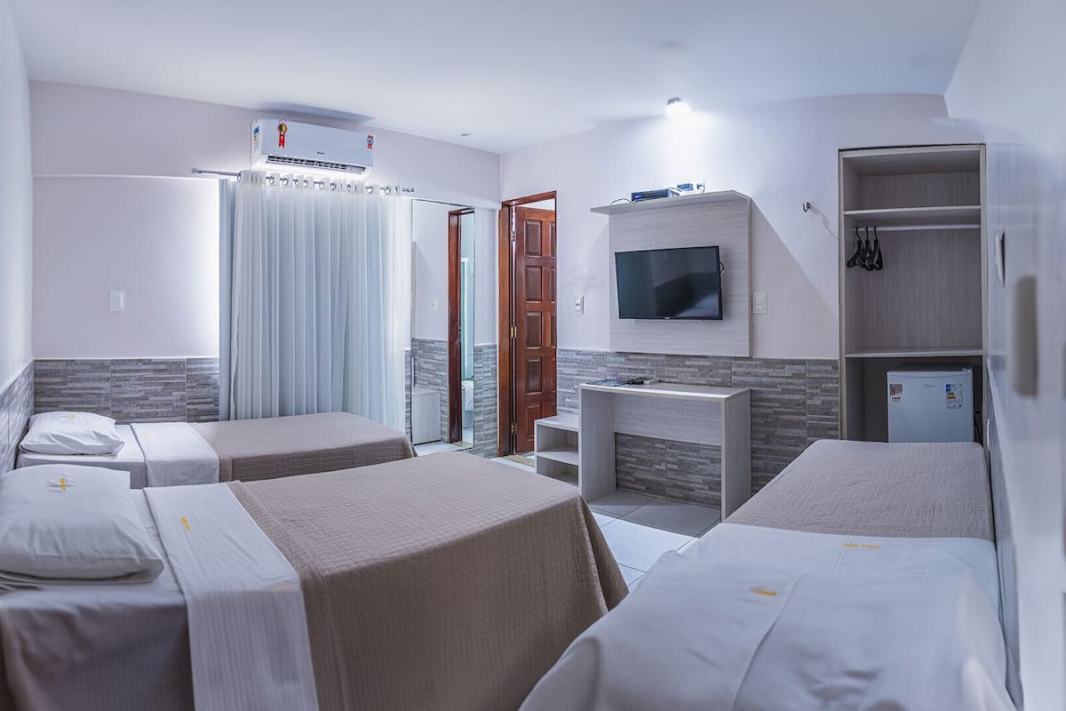 Ein Hotelzimmer mit zwei Einzelbetten, einem an der Wand befestigten Fernseher, einem kleinen Schreibtisch und einem Kleiderschrank.