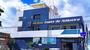 Ein Hotel namens 'Hotel Pousada Costa do Atlântico' mit modernem Design, das eine auffällige blaue Fassade und einen gut sichtbaren Eingang zeigt.