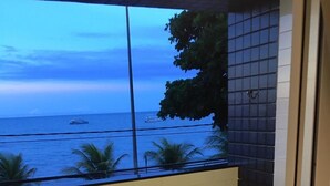 Ein Balkon mit zwei Korbstühlen, einer mit Blumenkissen und der andere mit gemustertem Kissen. Der Balkon bietet Blick auf ein Gewässer mit Booten und Palmen.
