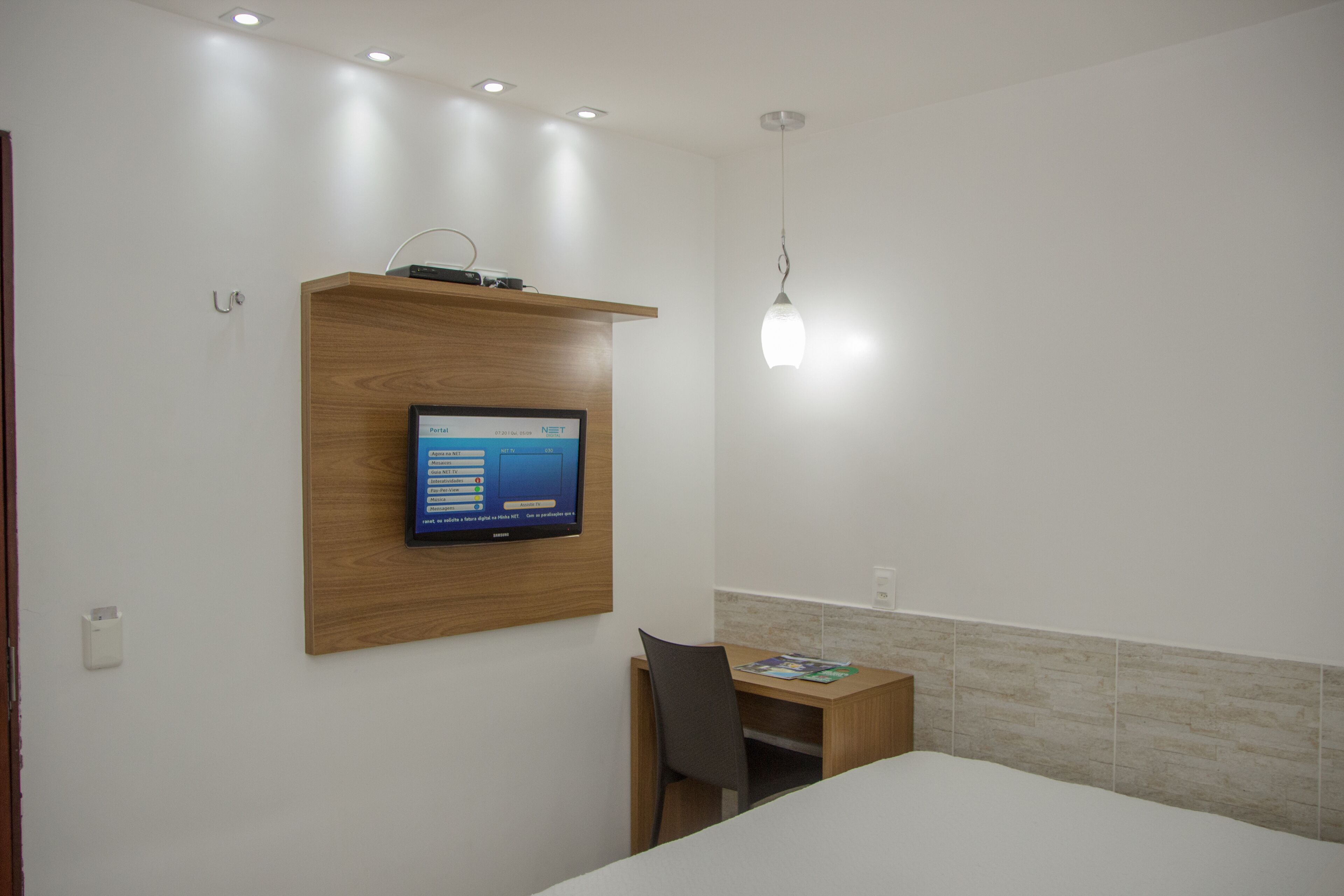 Hotelkamer met een bed, een bureau met stoel, een wandtelevisie en een wandplank.